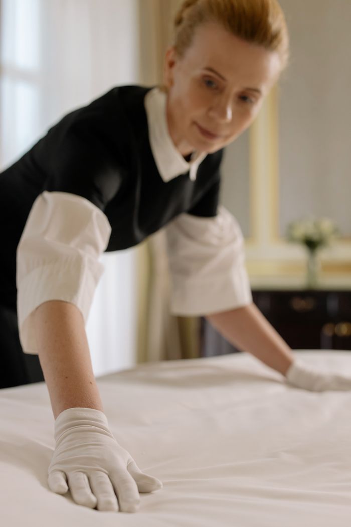 A housekeeper gracefully smooths and arranges bed linens in a luxury hotel room, highlighting hospitality know-how.